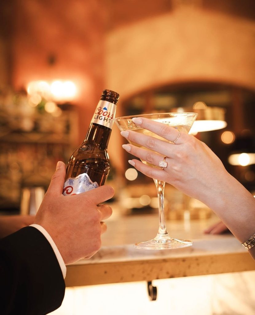 Newlyweds toast with beer bottle and champagne flute, engagement ring visible on bride's hand