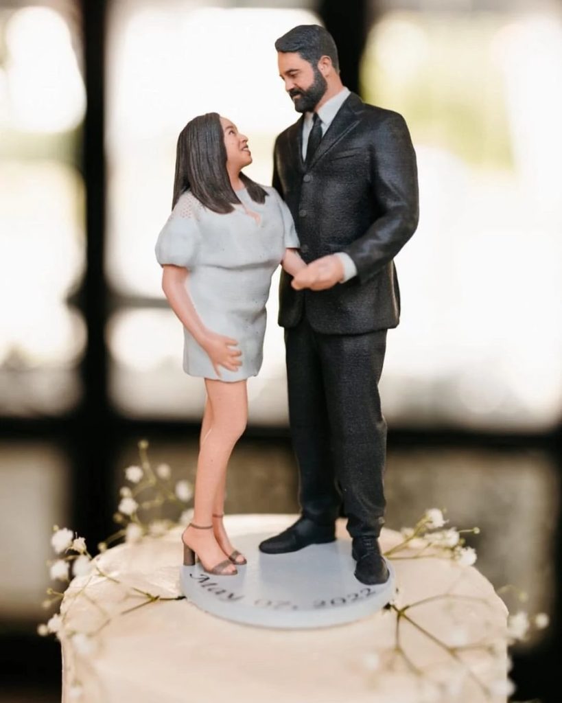 Custom 3D-printed miniature figurines of a couple atop a wedding cake, showcasing personalized cake topper design