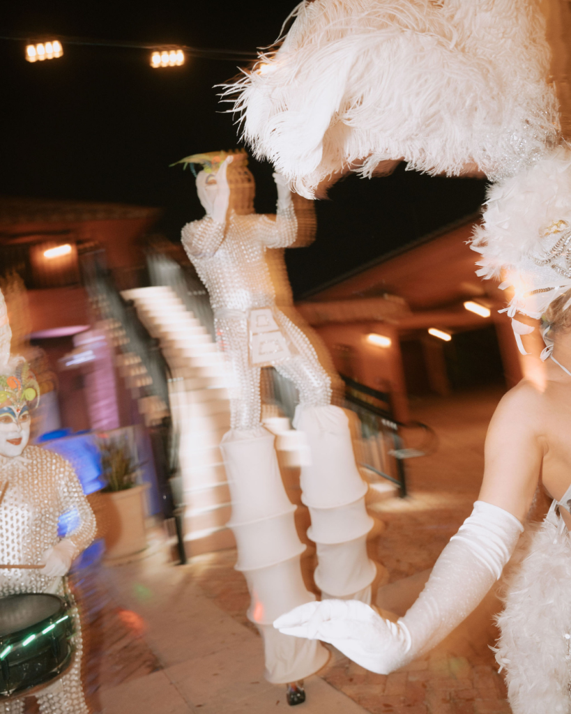 Bride in feathered dress dancing at festive reception with vibrant lighting