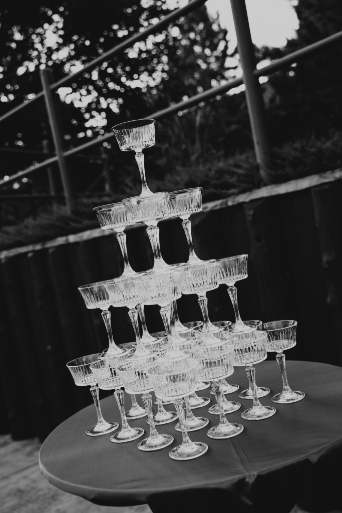 Tiered champagne tower with vintage coupe glasses arranged on round table outdoors in black and white