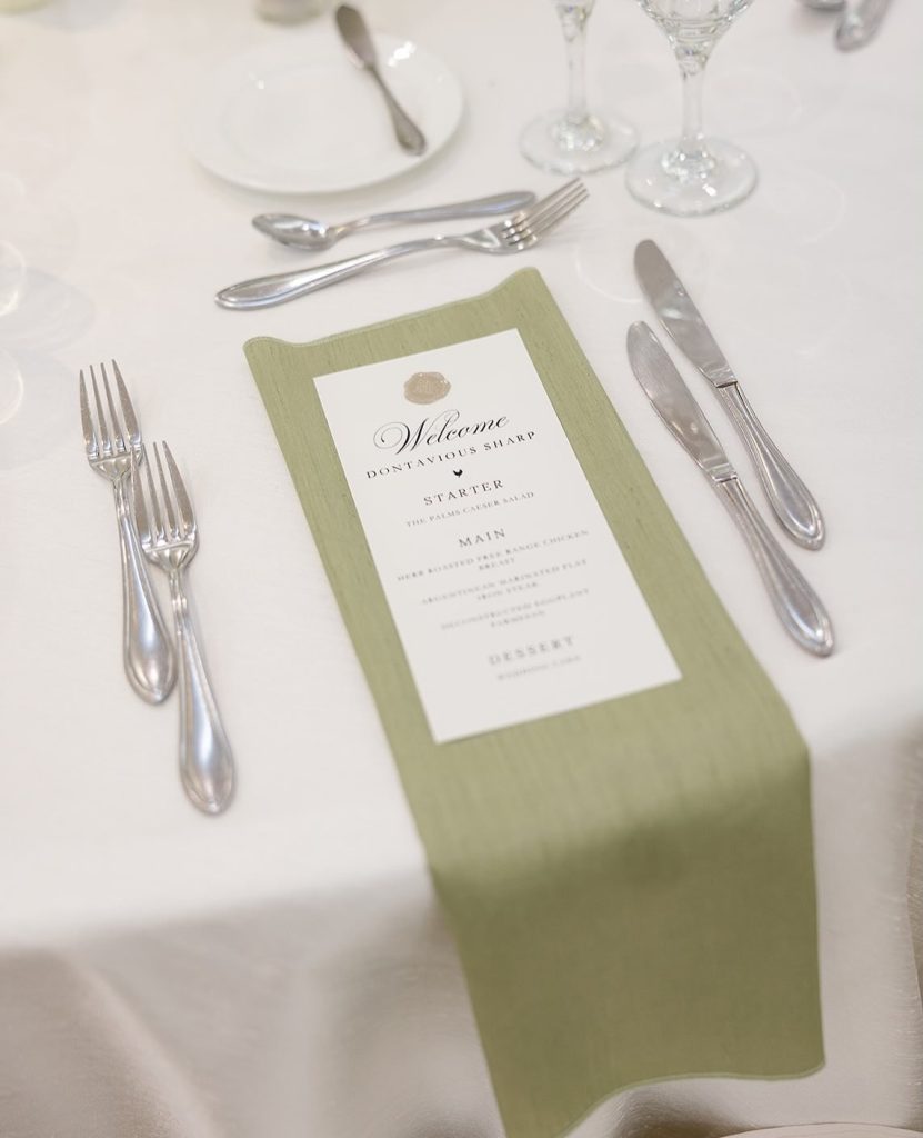 Elegant place setting with sage green napkin and printed menu card flanked by silver flatware