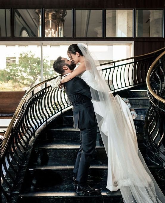 Bride and groom sharing romantic kiss on curved staircase with flowing veil cascading down steps