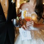 Bride and groom hold personalized monogrammed cocktail napkins with specialty drinks at wedding reception