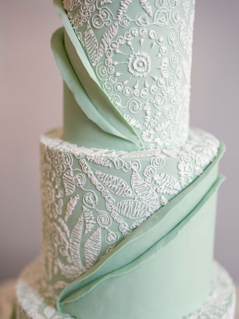 Mint green tiered wedding cake with intricate white lace piping and fondant draping
