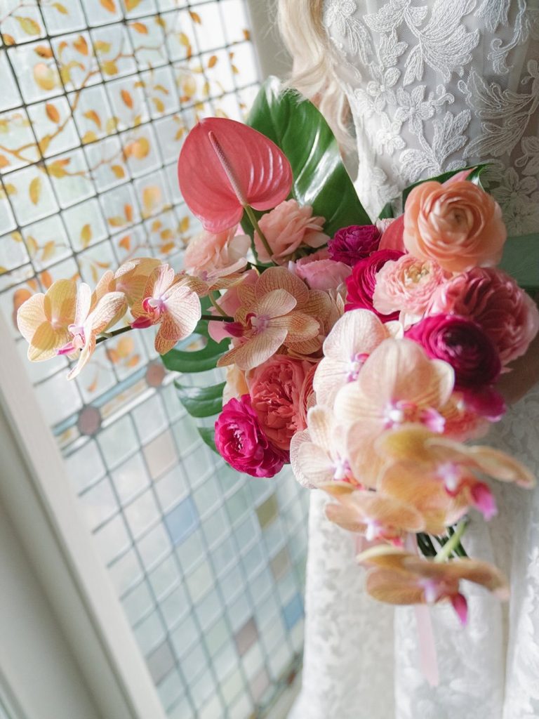 Bride holding vibrant tropical bouquet with orchids and colorful blooms against lace gown