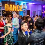 Guests dancing at party venue with illuminated marquee DANCE sign and colorful lighting