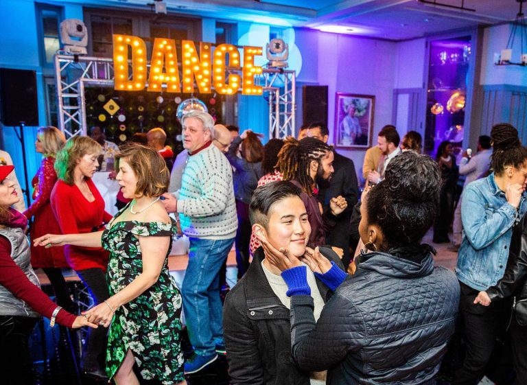 Guests dancing at party venue with illuminated marquee DANCE sign and colorful lighting