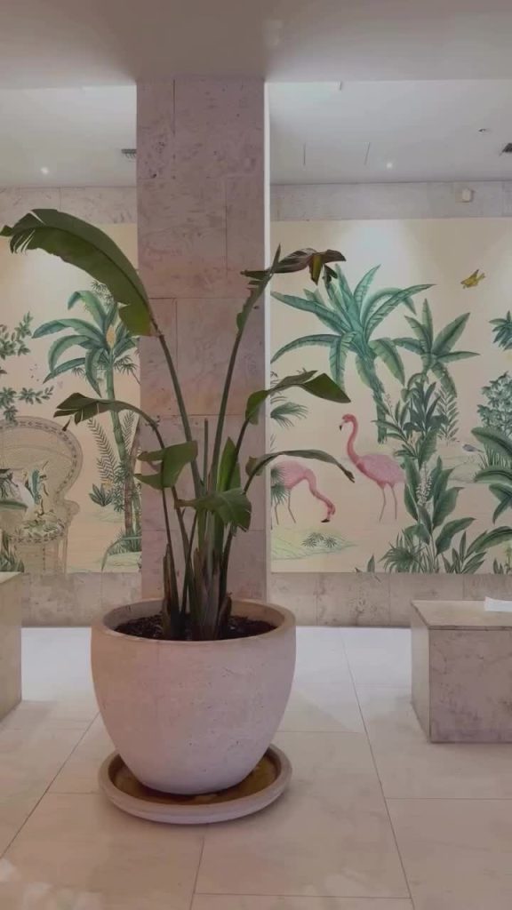 Potted tropical plant against decorative wall mural with flamingos and palm motifs