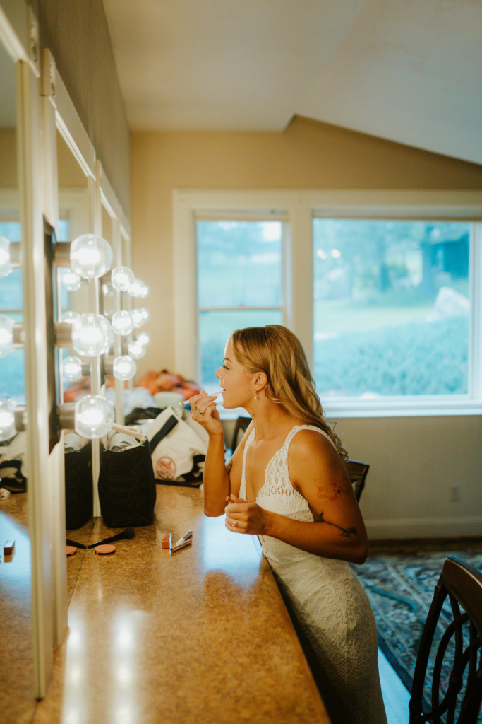 Bride Mallory applying makeup at vanity mirror during getting-ready preparations