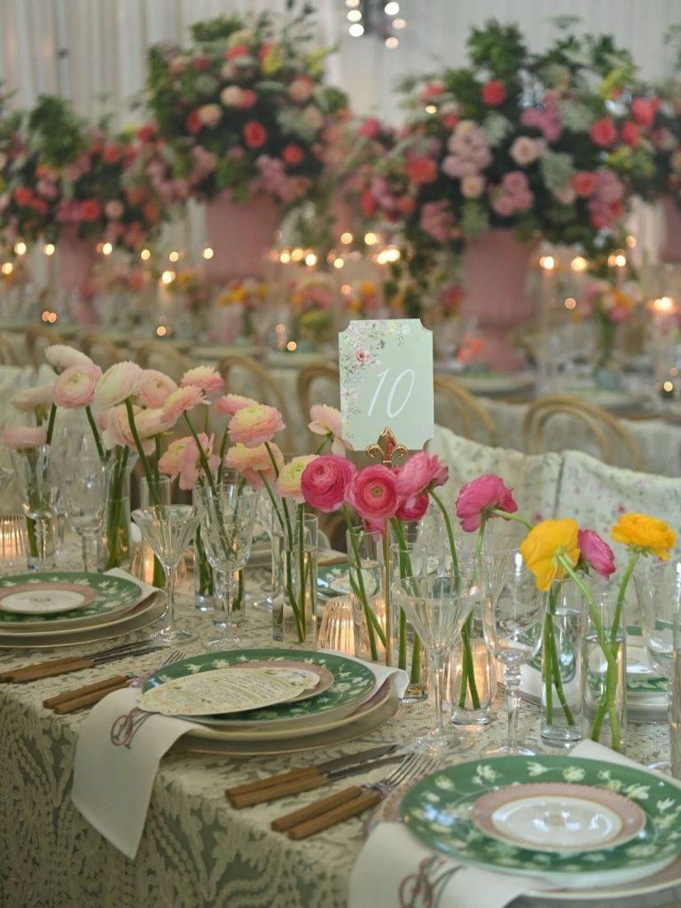 Reception table with pink and yellow blooms in glass vases, green plates, and table number ten