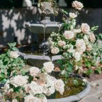 Tiered stone fountain adorned with blush and white roses in garden setting