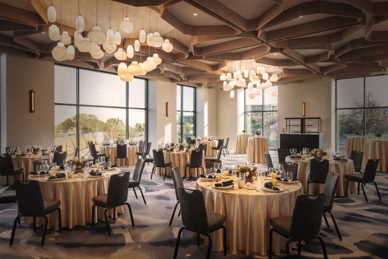 Elegant reception venue with marble tables, upholstered chairs, and modern lighting beneath tall windows