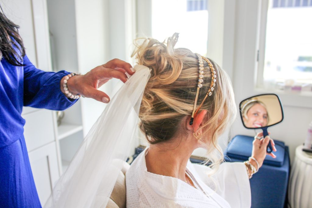Bride getting hair and makeup done while wearing white robe and veil in preparation for wedding day