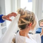 Bride getting hair and makeup done while wearing white robe and veil in preparation for wedding day