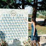 Woman in blue dress pointing to escort card display with blue agate slices and monogram, flanked by floral arrangements