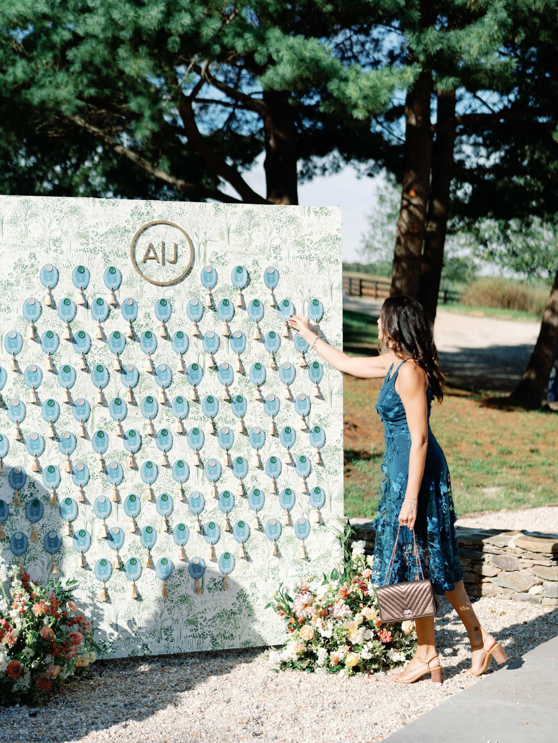 Woman in blue dress pointing to escort card display with blue agate slices and monogram, flanked by floral arrangements