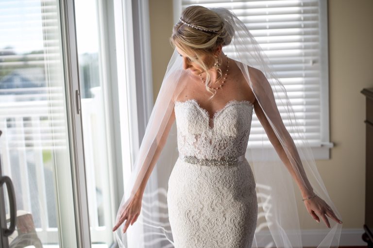 Bride in strapless lace wedding gown with crystal belt and cathedral veil, styled hair in elegant updo with jeweled headpiece