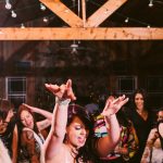 Wedding guests dancing enthusiastically in rustic barn venue with exposed beams and string lights
