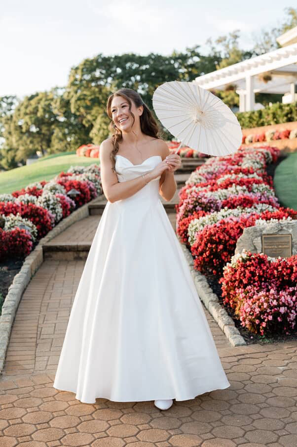 Bride in white ballgown holding bouquet among colorful mum displays at outdoor venue