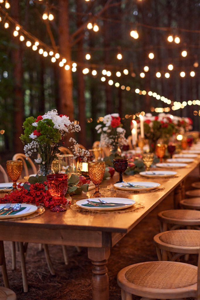Rustic outdoor reception table with string lights, floral centerpieces, and place settings at dusk