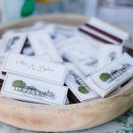 Personalized wedding favor matchboxes in wooden bowl displaying venue illustration and couple's names with date