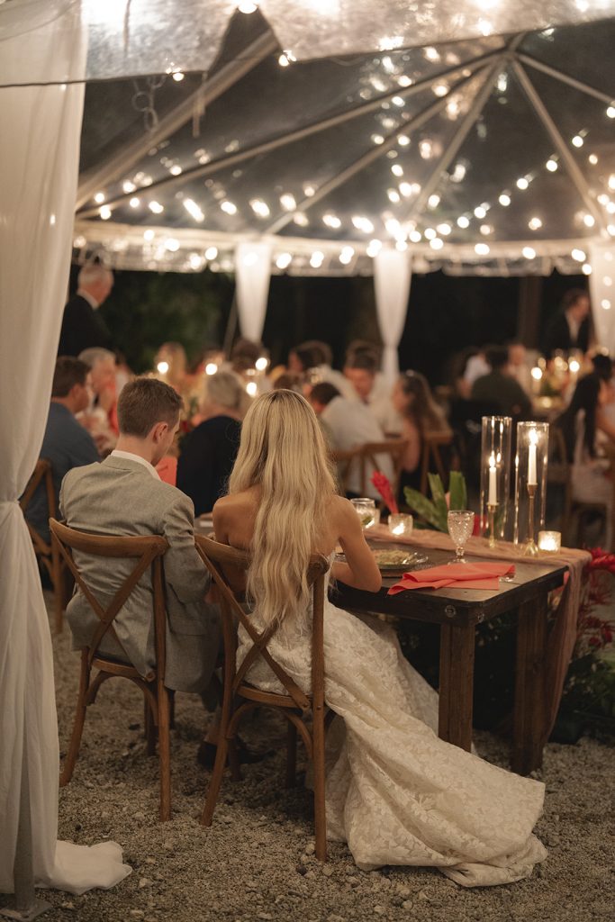 Bride and groom seated at candlelit reception table under string lights