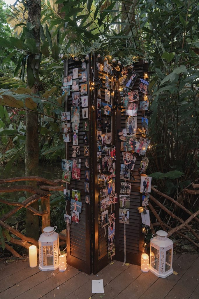 Wooden photo display with family pictures illuminated by string lights and white lanterns in tropical garden setting