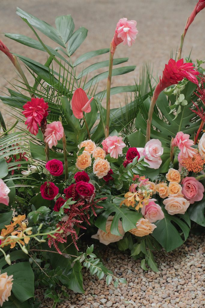 Vibrant tropical floral arrangement with pink, burgundy, and peach blooms alongside palm fronds