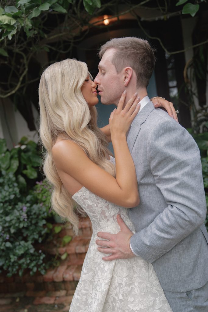 Newlyweds share intimate moment in garden courtyard surrounded by lush greenery and brick pathway
