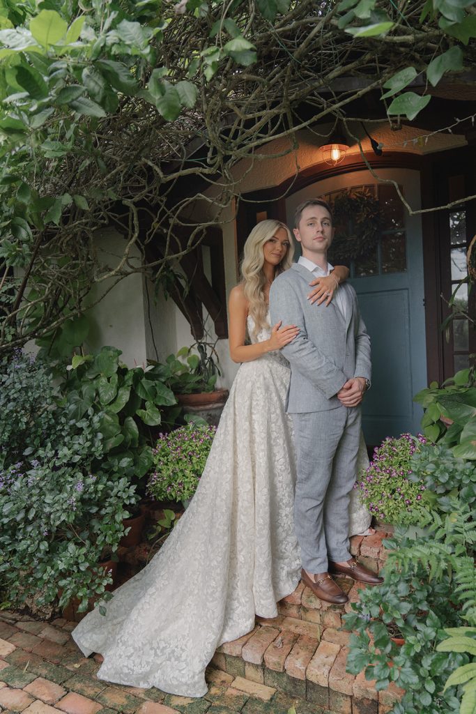 Bride and groom embrace beneath vine-covered archway at garden venue entrance