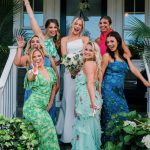 Bride and bridesmaids celebrating on front porch in colorful tropical-themed dresses