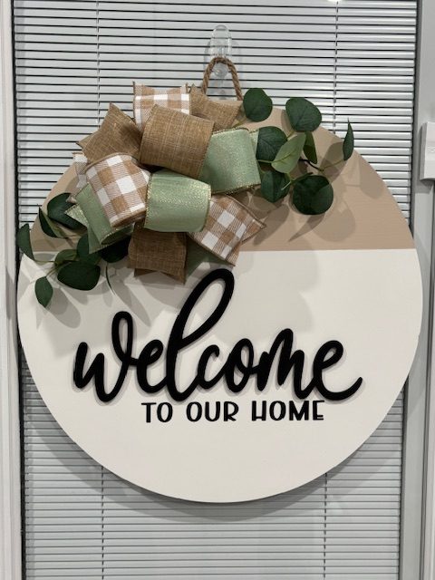 White round door hanger reading "Welcome to our home" with eucalyptus and neutral burlap ribbon accents