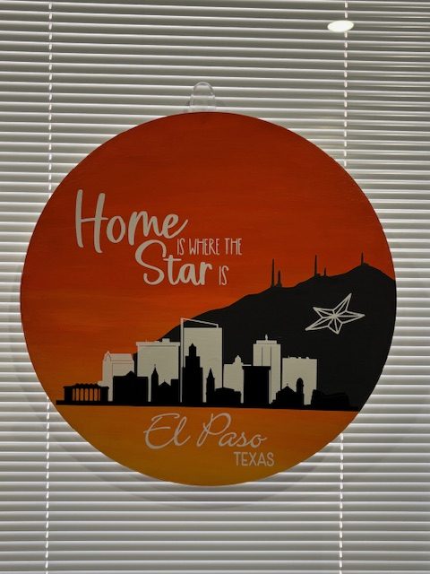 Round orange door hanger with El Paso skyline silhouette and "Home is where our story starts" text