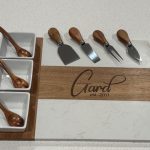 Personalized cheese board set with marble and wood surface, wooden-handled utensils, and three ceramic compartments with spoons