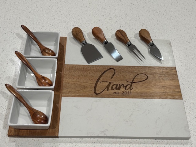 Personalized cheese board set with marble and wood surface, wooden-handled utensils, and three ceramic compartments with spoons