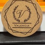Cork coaster with Valencia monogram featuring letter V in laurel wreath and geometric border