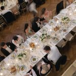 Overhead view of formal wedding reception with guests seated at long tables featuring white linens, floral centerpieces, and candlelight