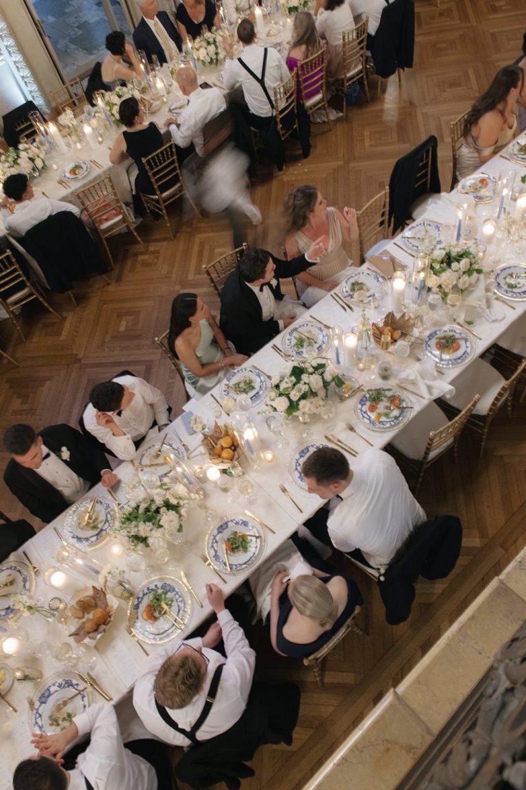 Overhead view of formal wedding reception with guests seated at long tables featuring white linens, floral centerpieces, and candlelight