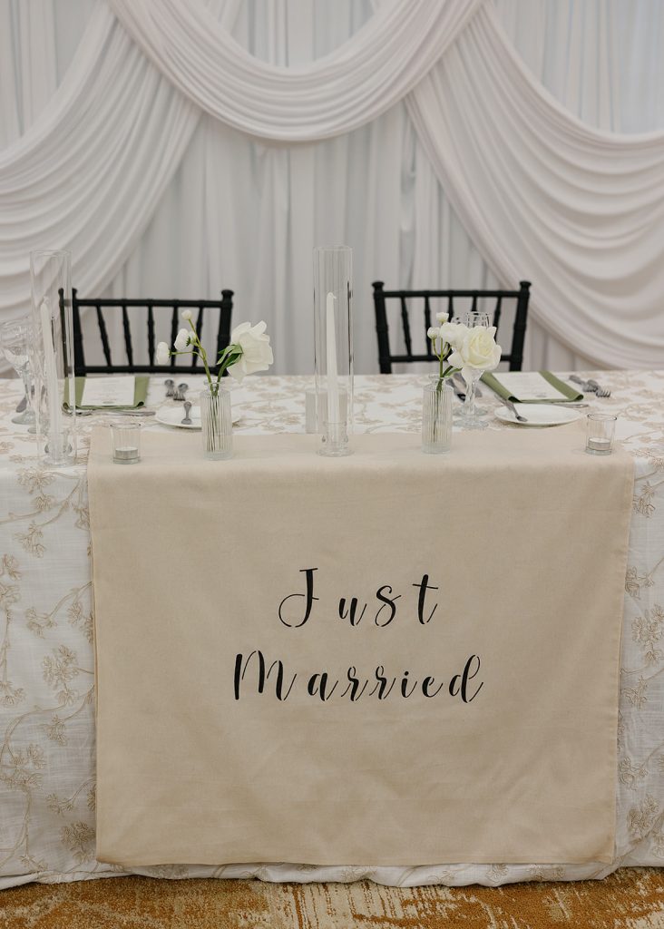 Sweetheart table with Just Married sign, white draping, and minimalist floral centerpieces