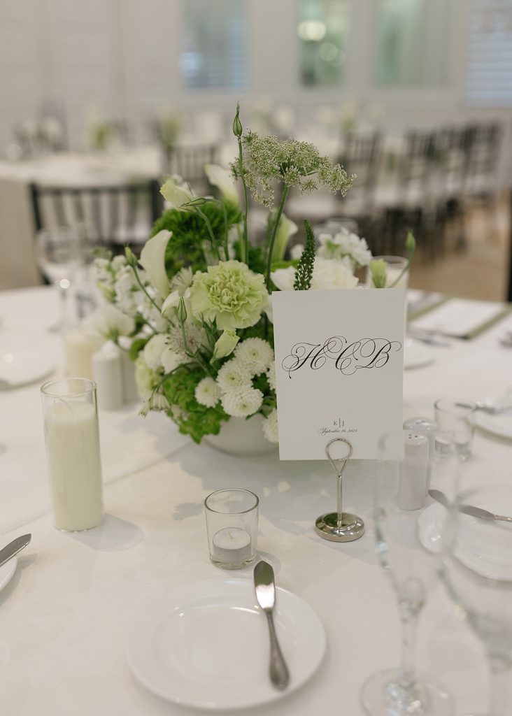 Elegant white and green centerpiece with monogrammed table card displayed on formal reception table
