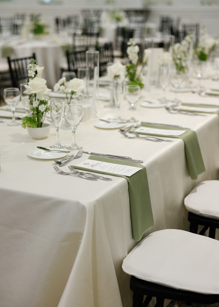 Elegant reception tables with white linens, green runners, and small floral arrangements