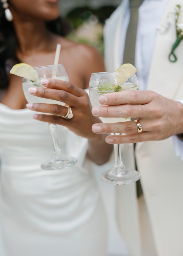 Bride and groom toasting with lemon-garnished cocktails, showcasing their wedding rings