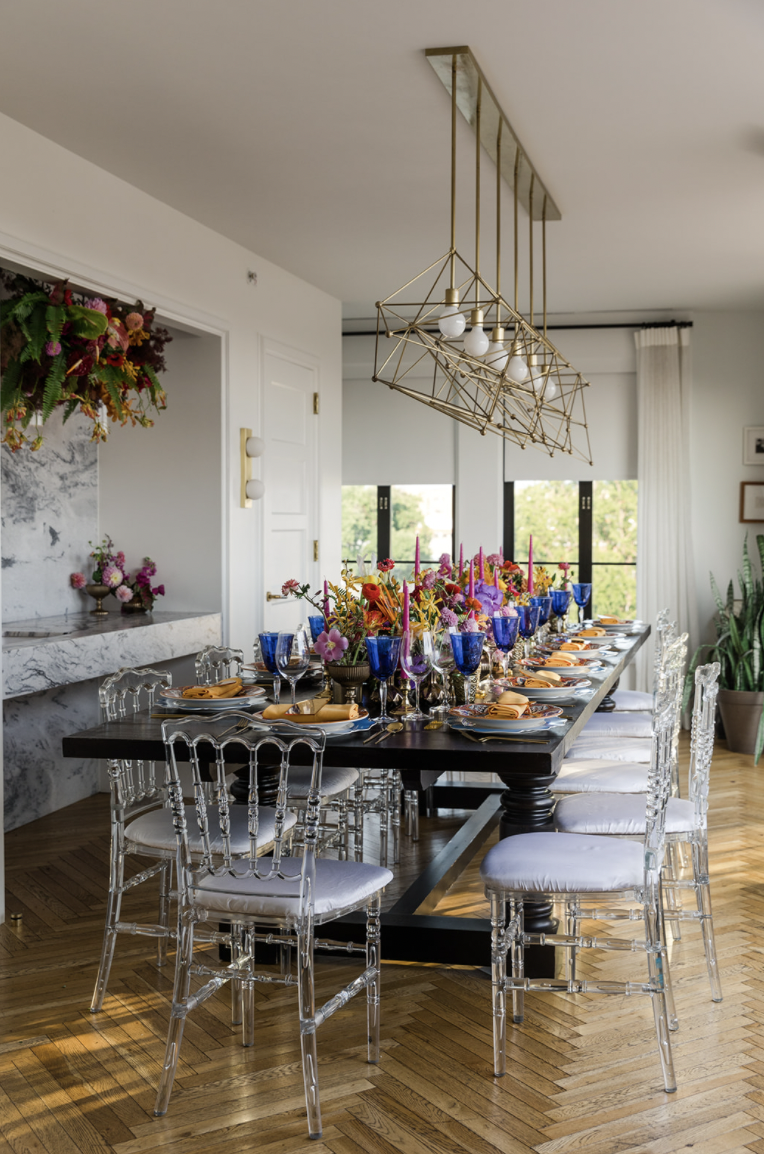 Elegant reception table with clear ghost chairs, tall candles, and colorful floral centerpieces