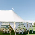 Elegant white tent with flowing drapes, gold chiavari chairs, and reception tables on manicured lawn