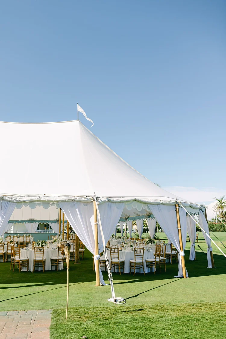 Elegant white tent with flowing drapes, gold chiavari chairs, and reception tables on manicured lawn