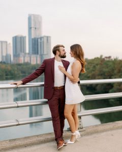 Couple embraces on bridge overlooking St. Louis skyline during engagement session