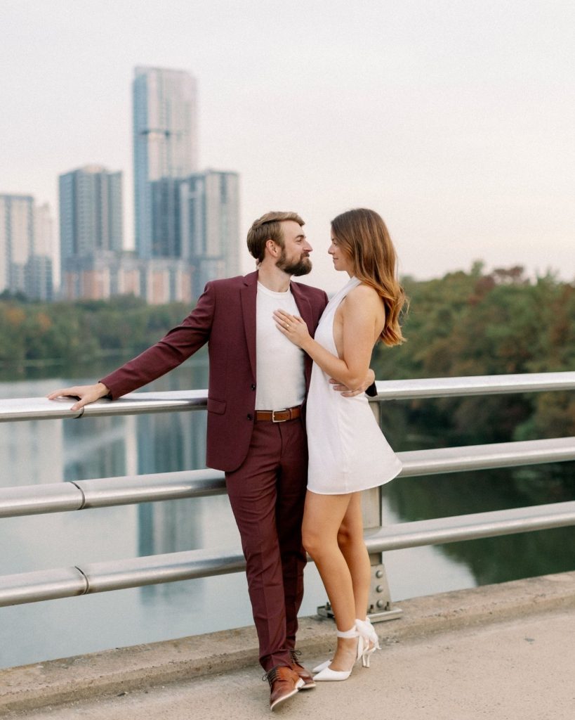 Couple embraces on bridge overlooking St. Louis skyline during engagement session