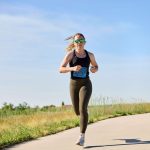 Fitness professional Madeline running in race bib on outdoor trail under clear blue sky