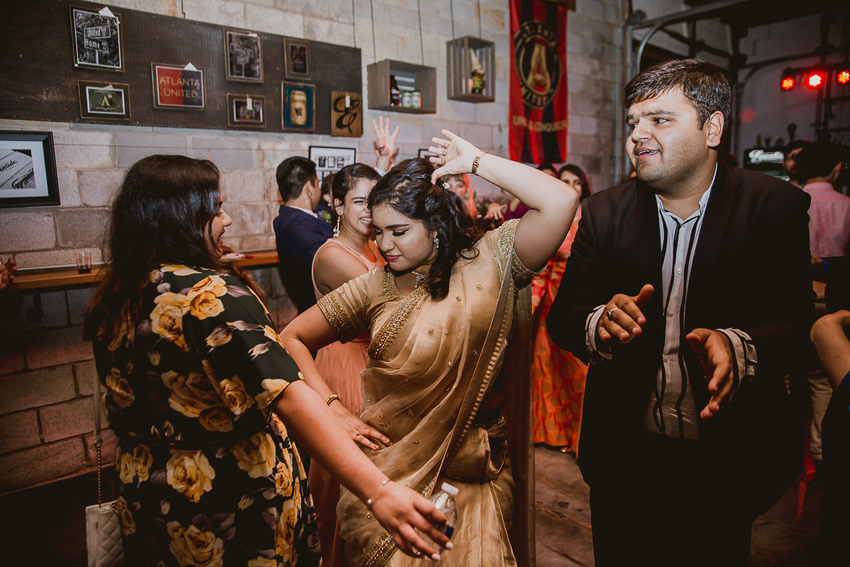 Wedding guests dancing together at reception venue with industrial brick walls and Atlanta United decor