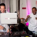 Two professional DJs performing together at wedding reception with pink ambient lighting